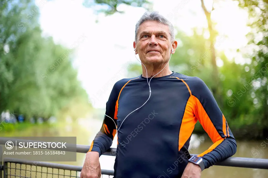 Retired senior man looking away while smiling against railing in park