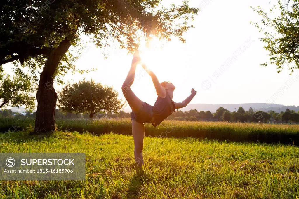 Teenage girl performing yoga in grassy field at sunset