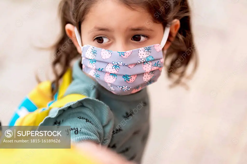 Girl with mask holding father's hand outdoors