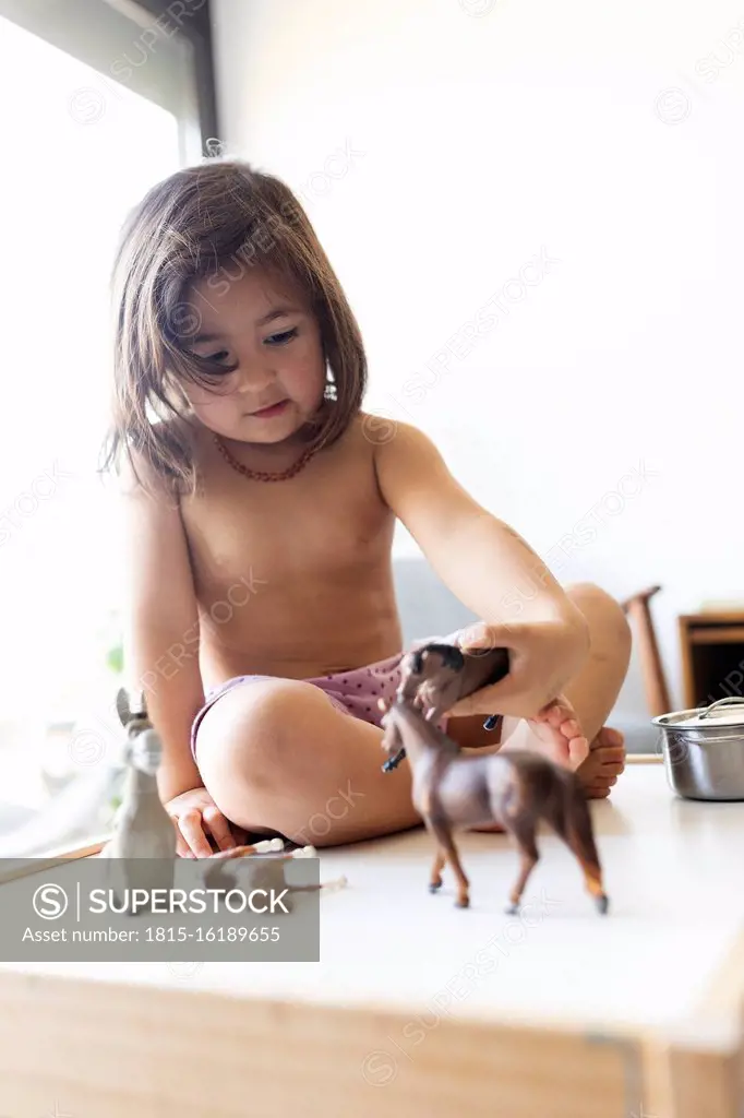 Portrait of shirtless little girl playing with toy horses