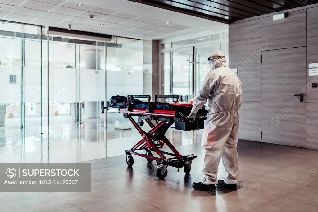 Ambulance, doctor wearing protective suit pushing empty stretcher