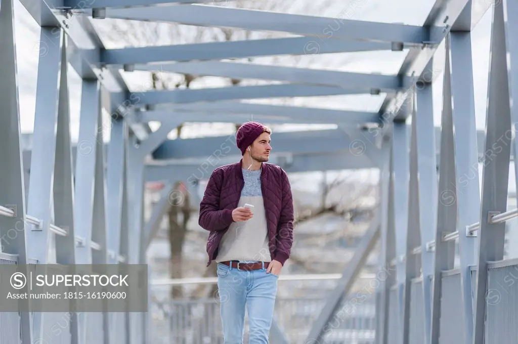 Young man walking on a bridge with earbuds and smartphone