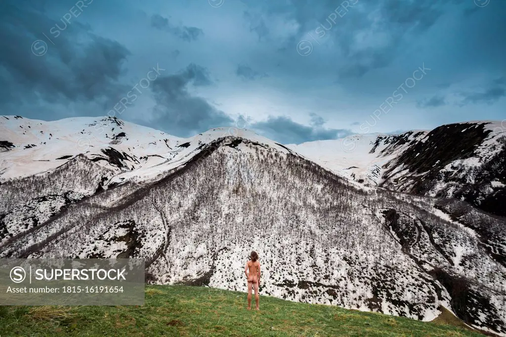 Georgia, Svaneti, Ushguli, Male nudist admiring snowcapped peaks in¶ÿCaucasus Mountains