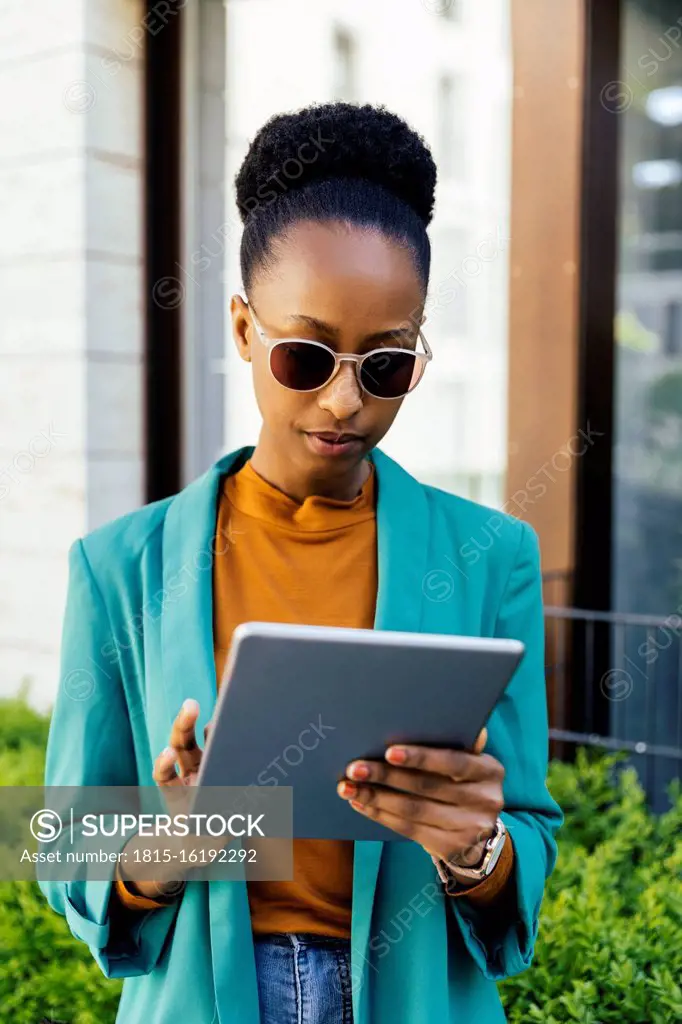 Portrait of young businesswoman wearing sunglasses using digital tablet outdoors
