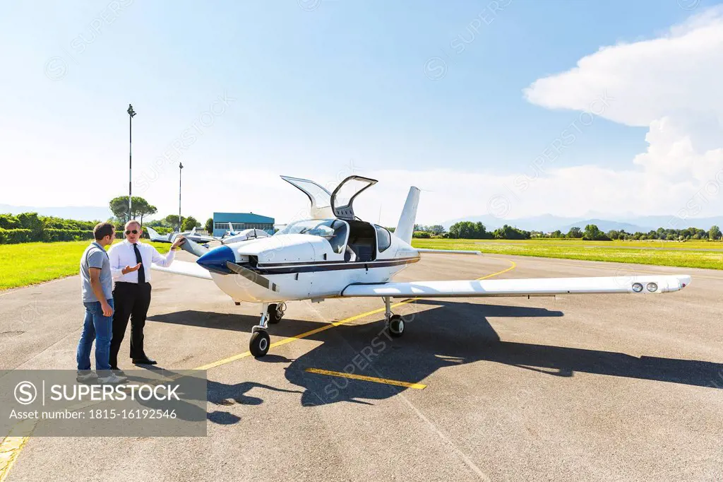 Pilot and Co-pilot satning on runway, talking in front of sports plane