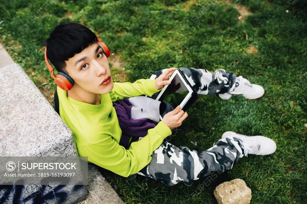 Young man wearing headphones using digital tablet while sitting on grassy land