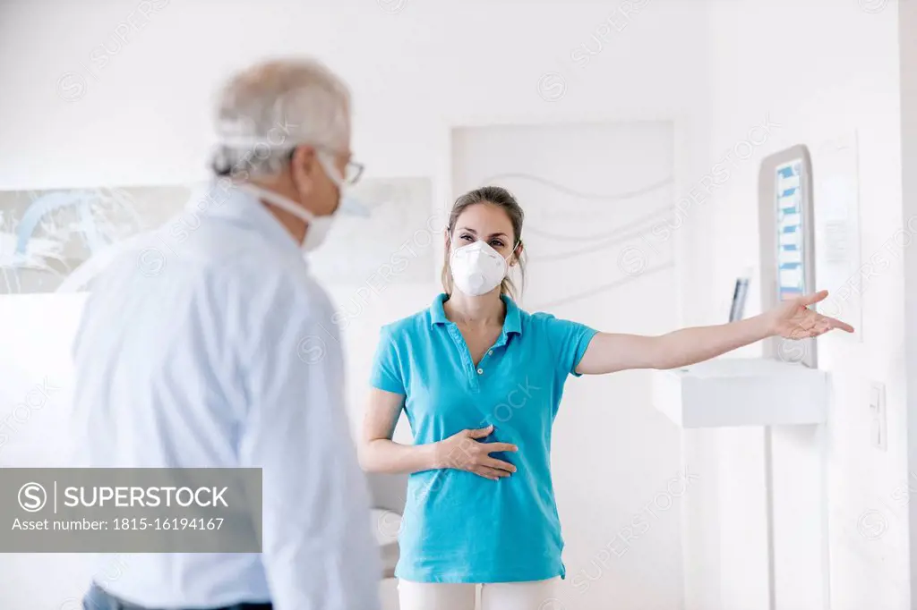 Senior man meeting his femal physiotherapist at the reception, wearing face masks