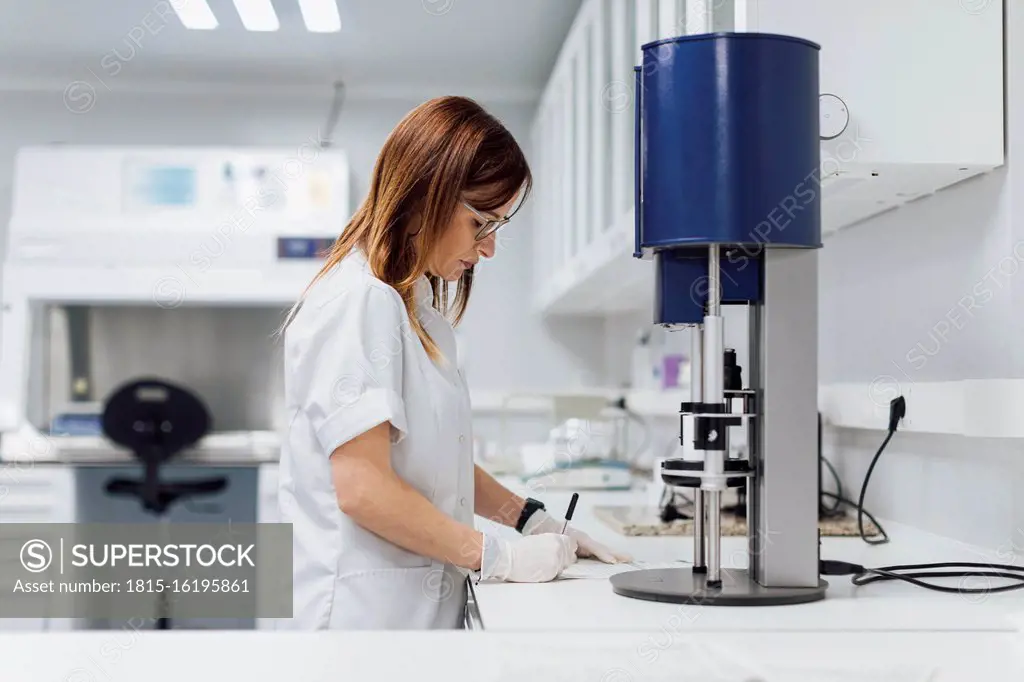 Confident mature female healthcare worker writing data at laboratory desk