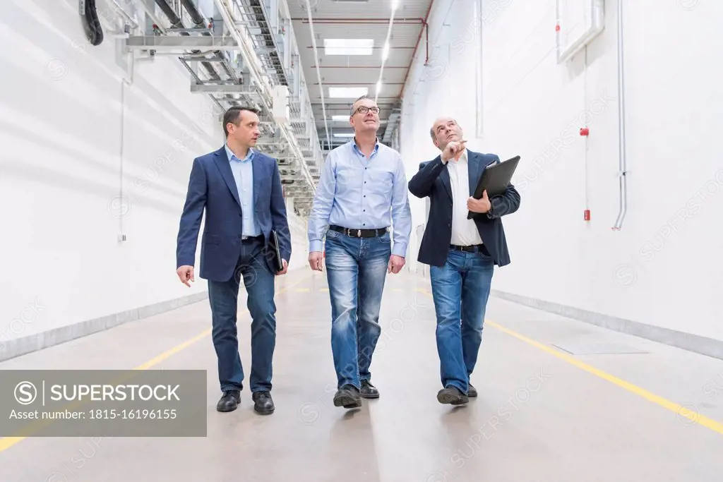 Three businessmen walking and talking on factory corridor