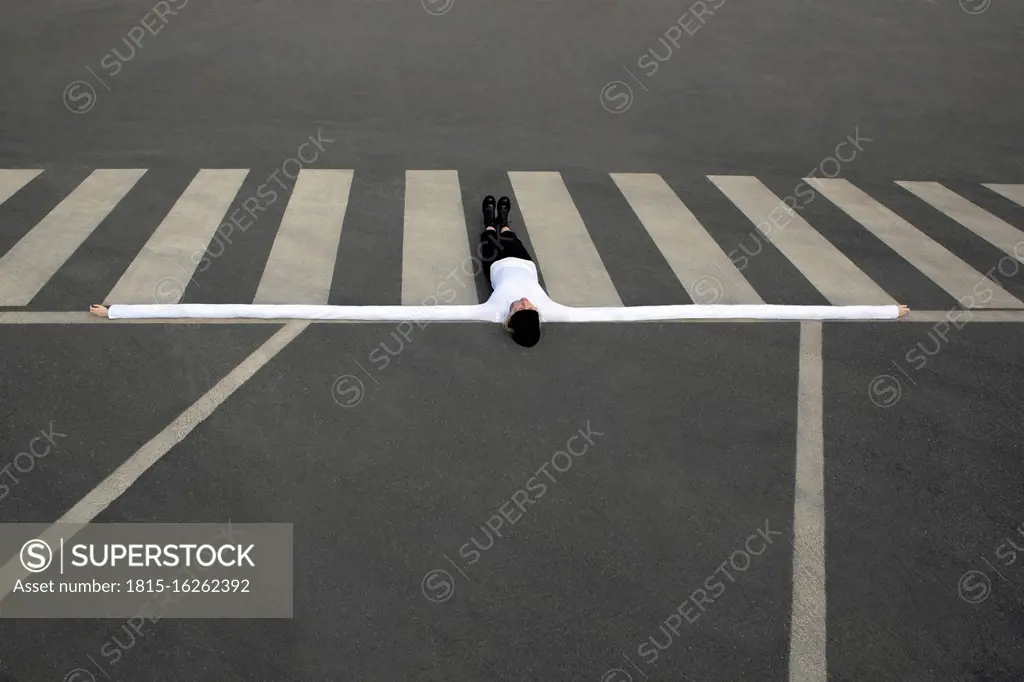 Woman with artificial long hands lying on zebra crossing