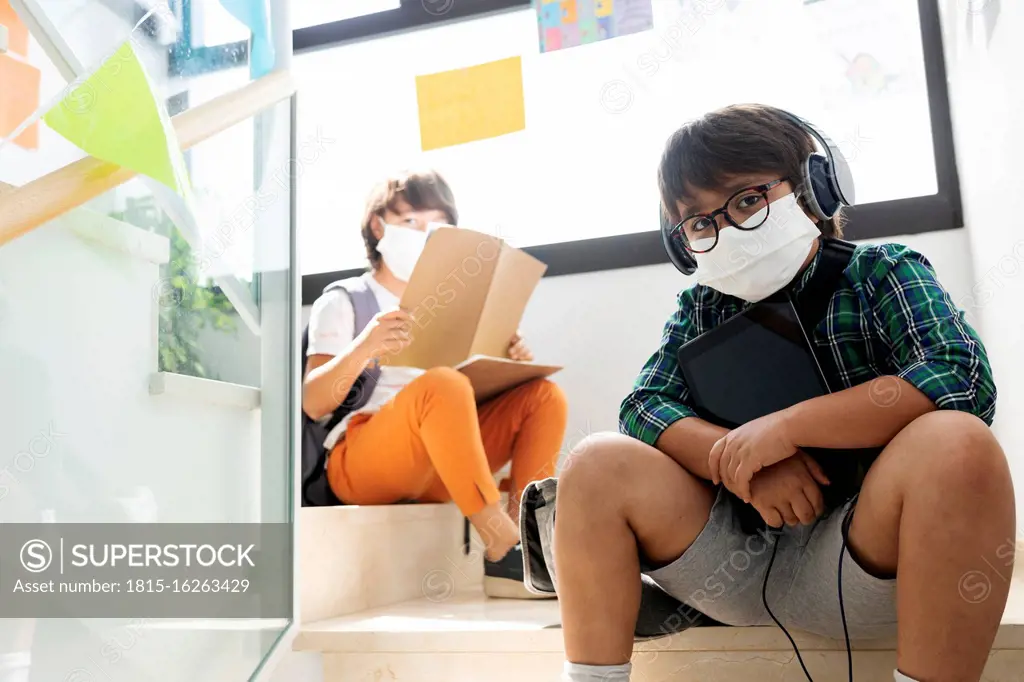 Boys wearing masks sitting at distance on steps in school