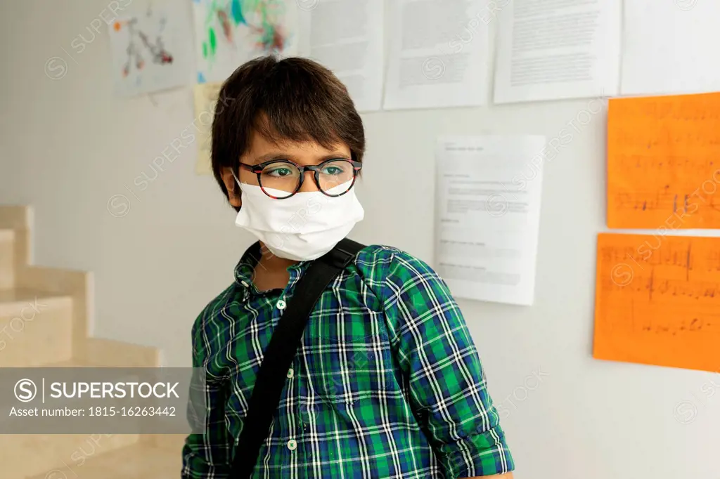 Boy wearing mask looking away while standing against wall in school