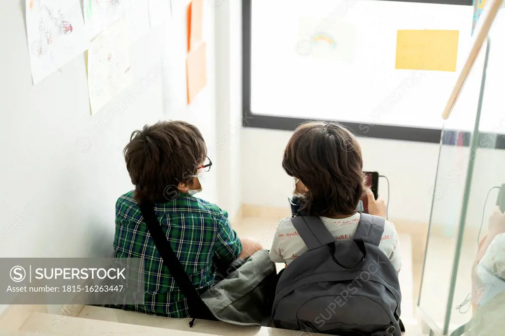 Boys wearing masks talking while sitting on steps in school