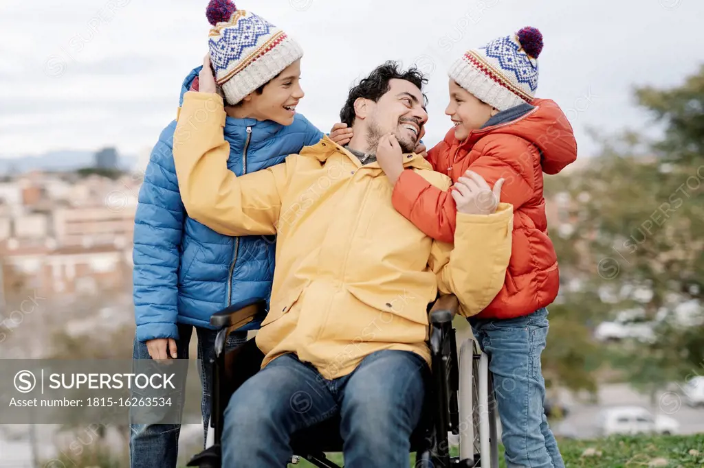 Loving father embracing sons while sitting on wheelchair in park