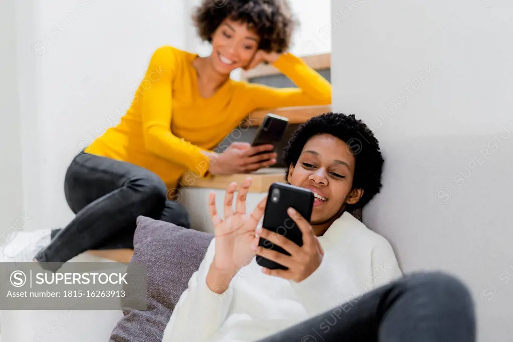 Two young women relaxing at home using their smartphones