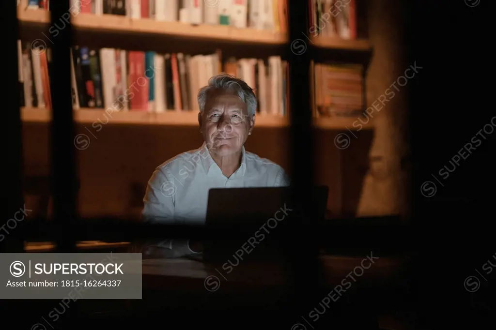 Senior businessman sitting in office, working late, smiling