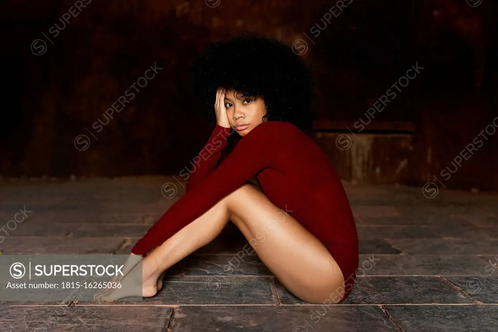 Young woman in red bodysuit sitting on ground