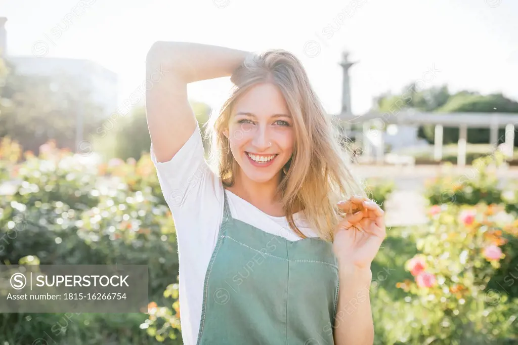 Portrait of happy young woman in public garden at backlight