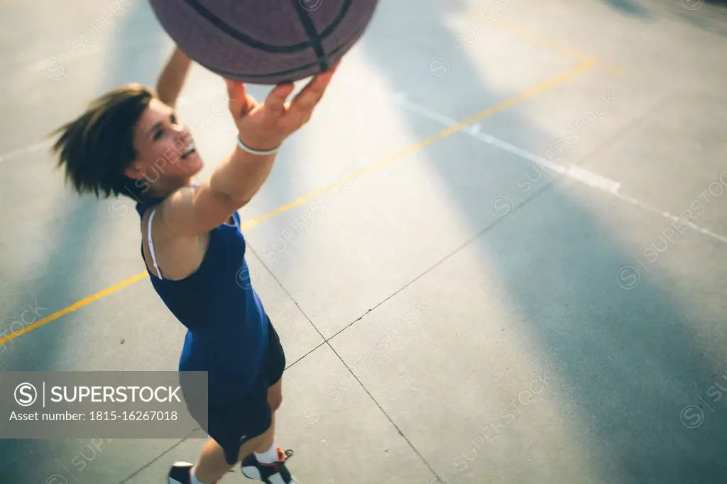 Teenage girl jumping while practicing basketball on court