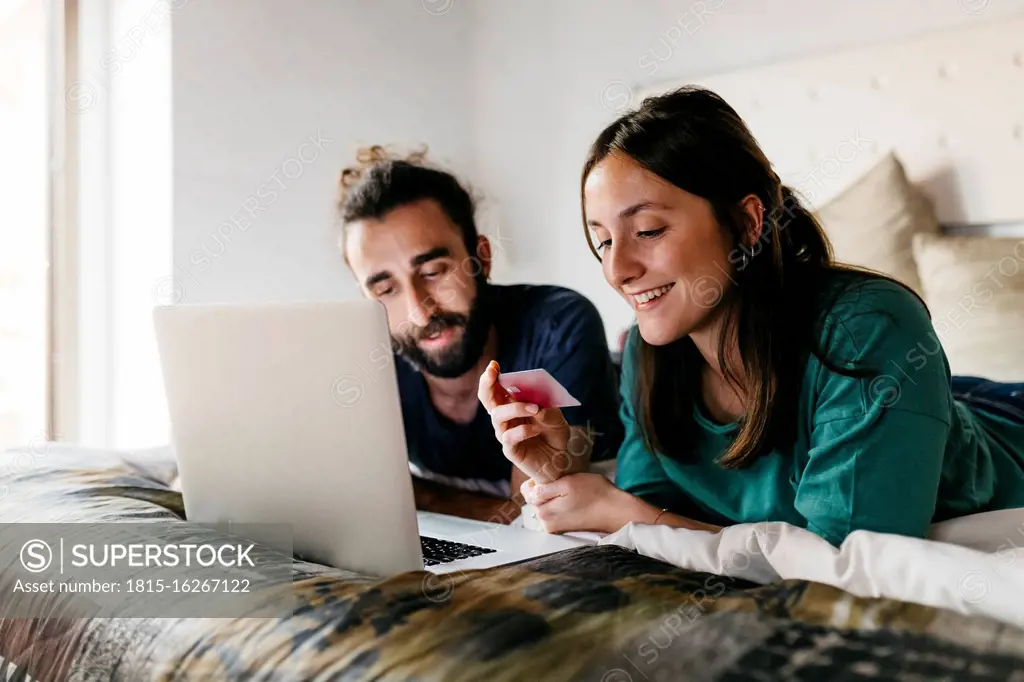 Happy couple lying on bed shopping online