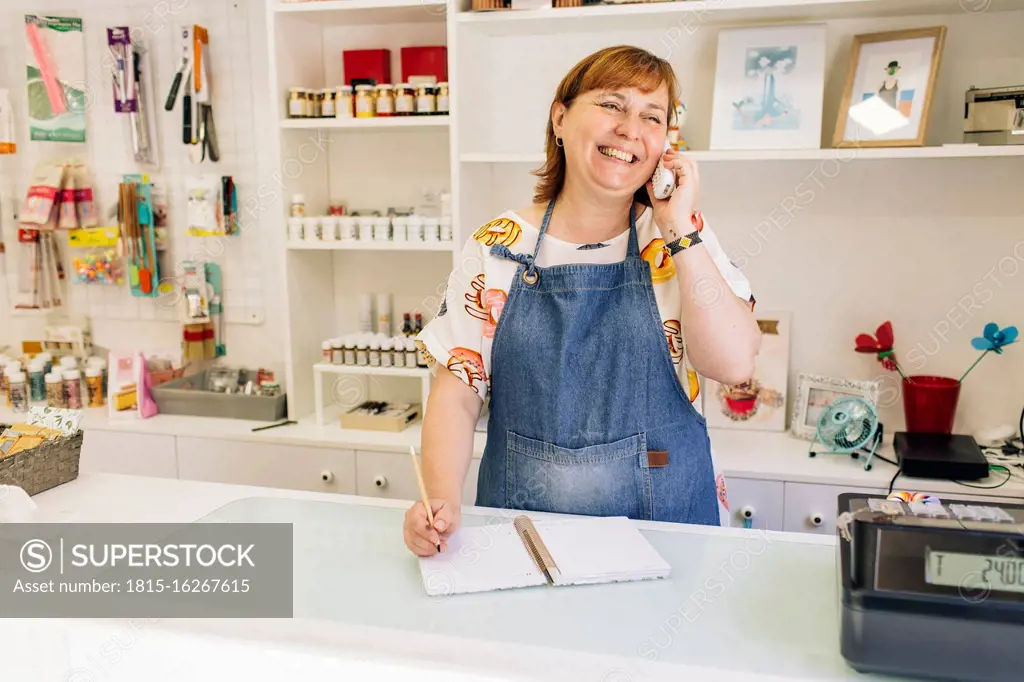 Smiling female baker taking order over phone in cake shop