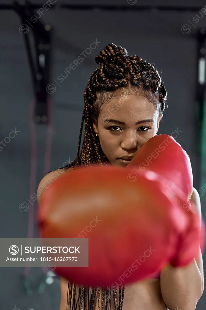 Confident young woman wearing red boxing gloves exercising in gym