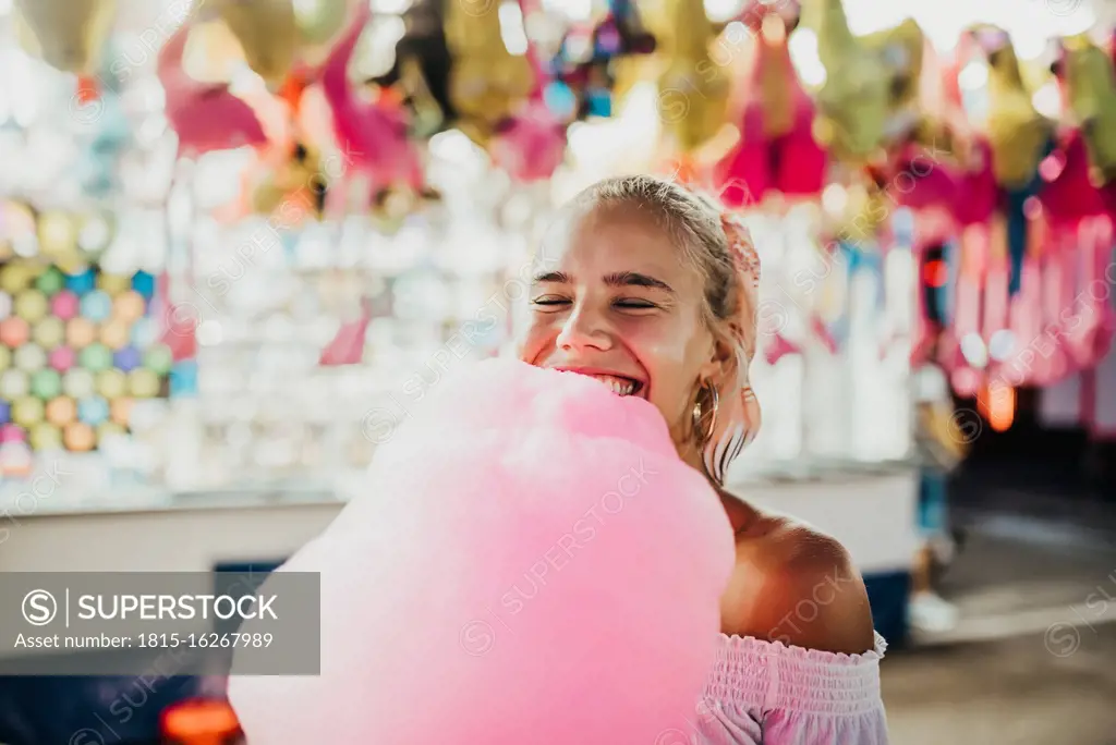 Close-up of smiling young woman with eyes closed holding cotton candy at amusement park