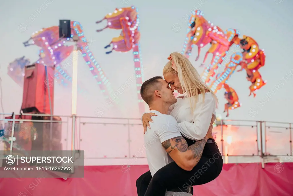 Romantic man carrying girlfriend while standing at amusement park