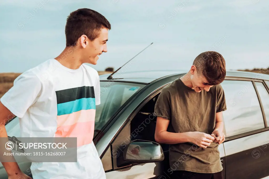 Male friends laughing while standing by car against sky at sunset