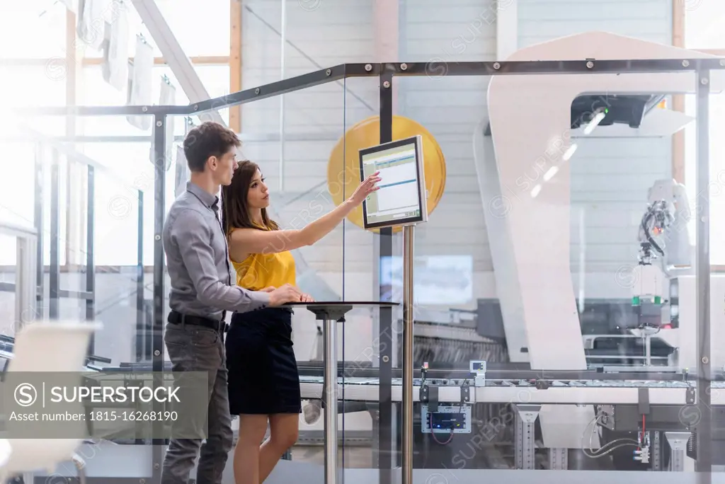 Business people discussing over computer while standing in factory