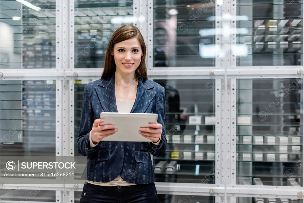 Smiling businesswoman using digital tablet while standing against glass in factory