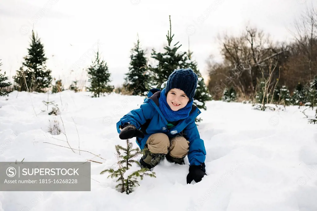 Smiling boy showing tree while crouching on snow covered land against sky