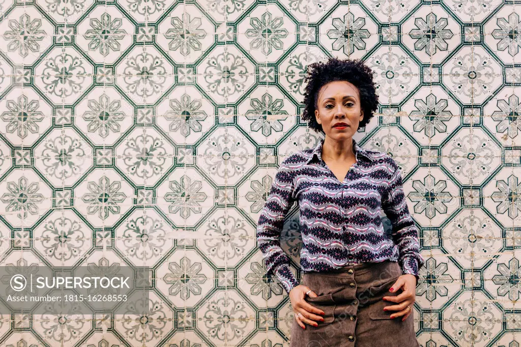 Stylish mid adult woman with curly hair standing against tiled wall