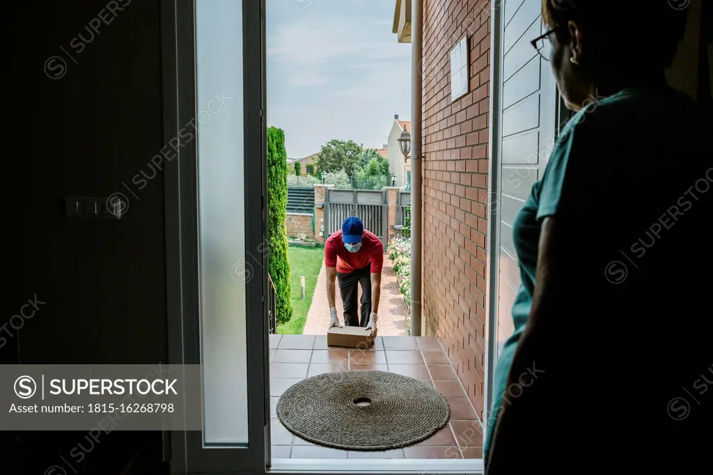 Senior woman looking at delivery person keeping package on front stoop