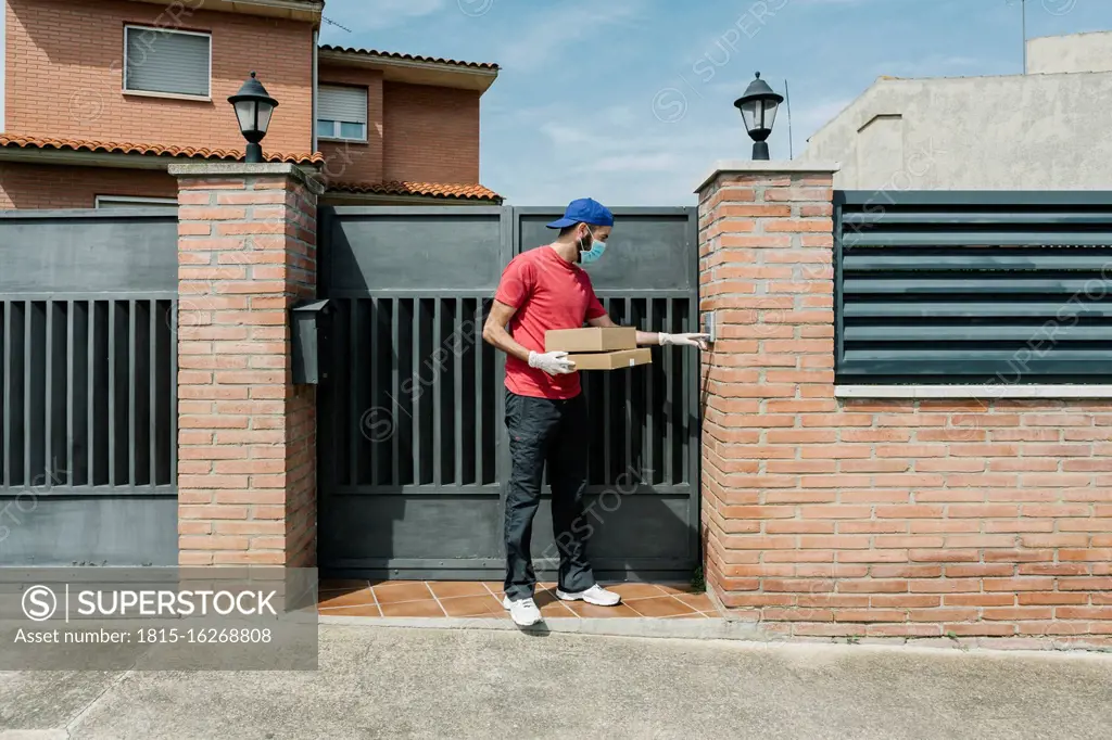 Male postal worker using intercom while standing with package at house gate