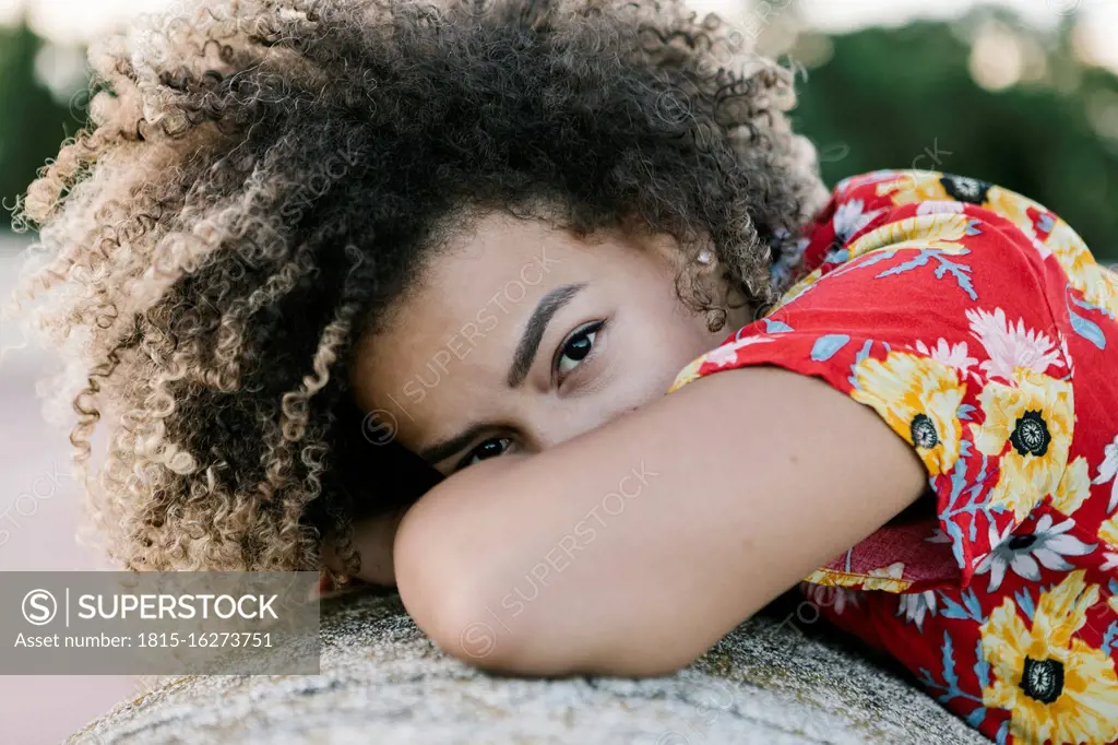 Confident young woman leaning on retaining wall during sunny day