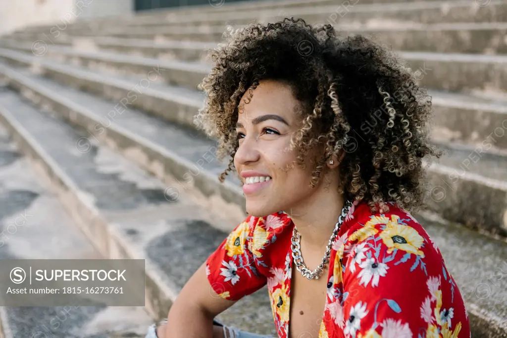 Thoughtful young woman smiling while sitting on steps during sunny day