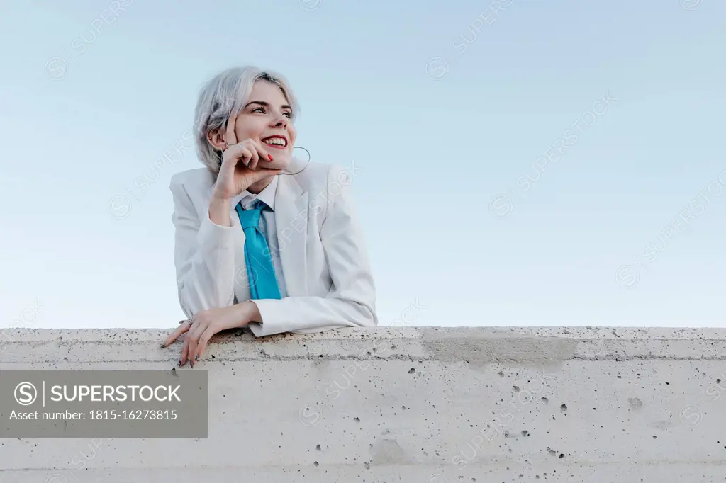 Smiling young woman wearing white suit standing by retaining wall against clear sky