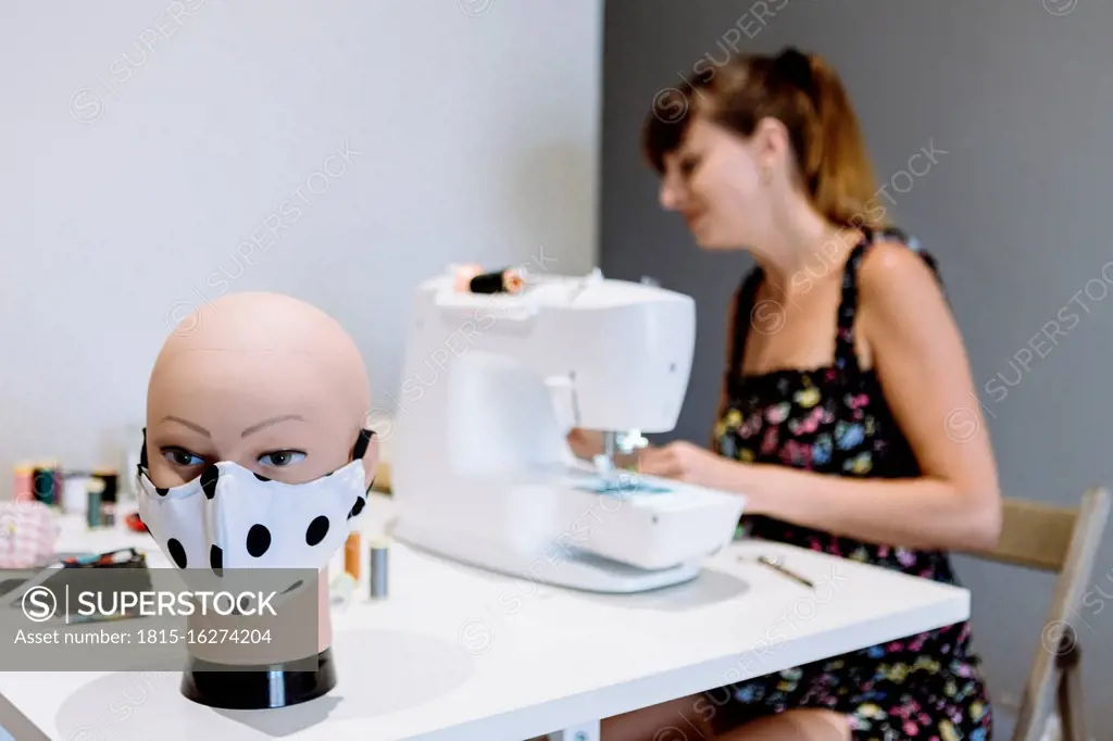 Close-up of mannequin with mask on table while female tailor working in background