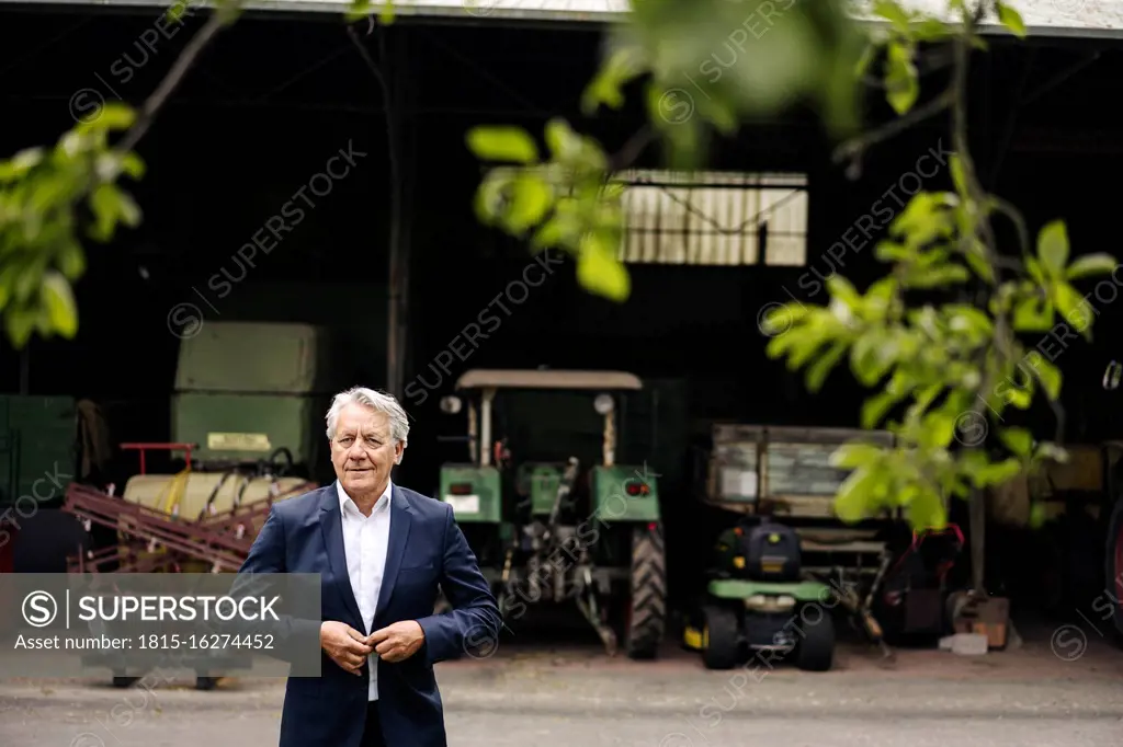 Senior businessman on a farm with tractor in barn