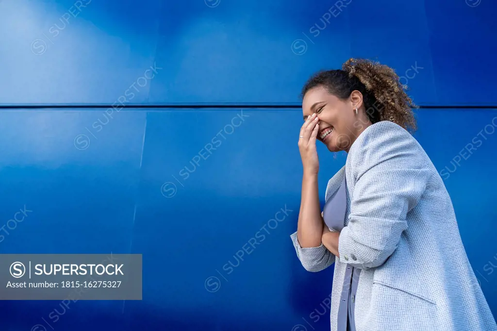 Laughing businesswoman in front of blue wall