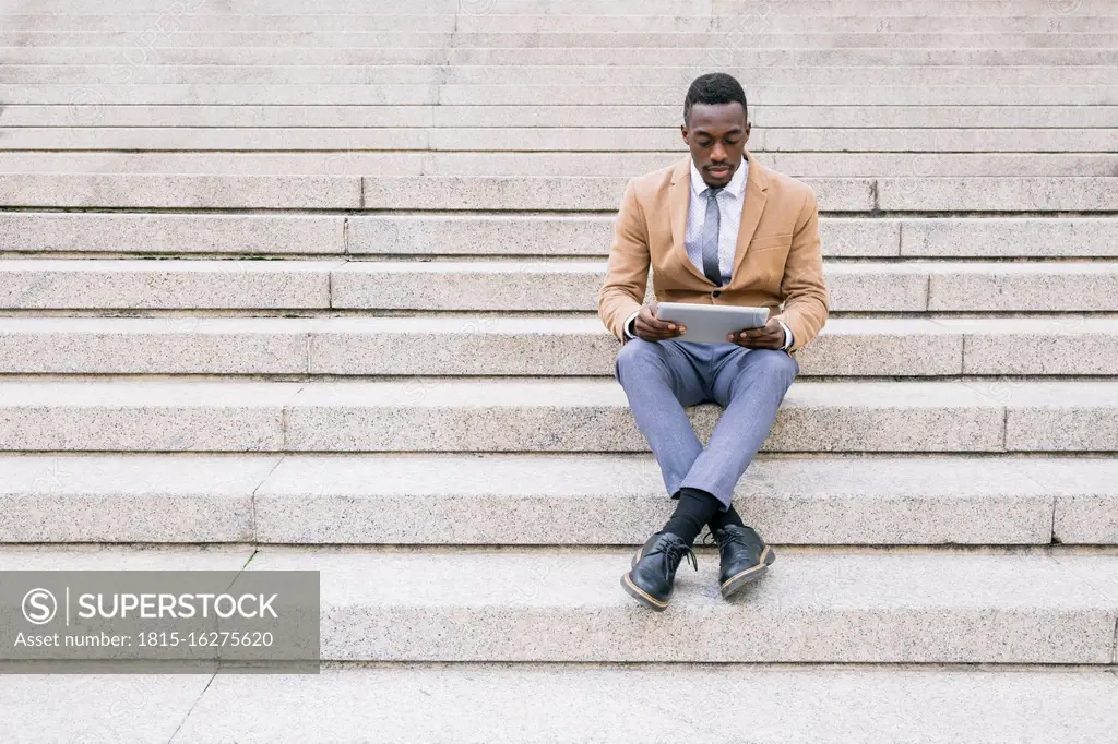 Young businessman sitting on stairs using a tablet