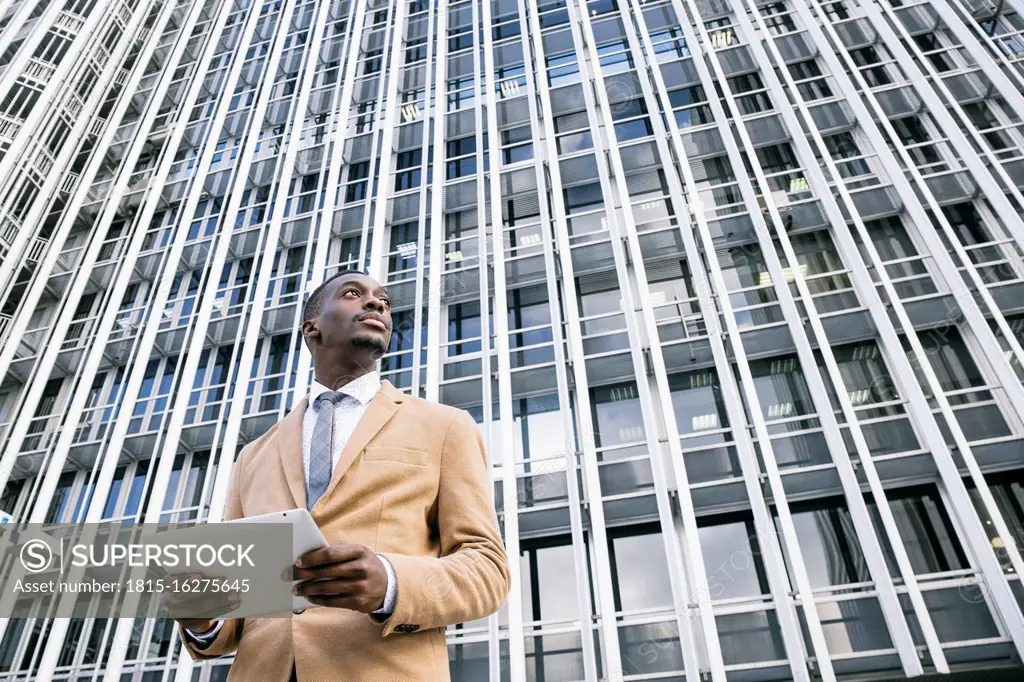 Young businessman in front of modern office building in the city holding a tablet