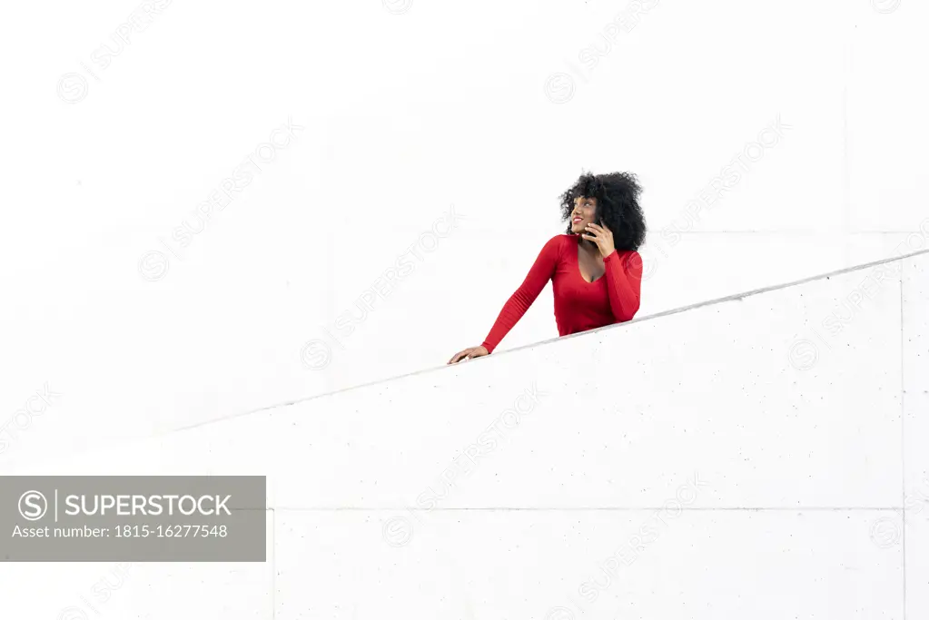 Young woman with afro hair using smartphone on white ramp