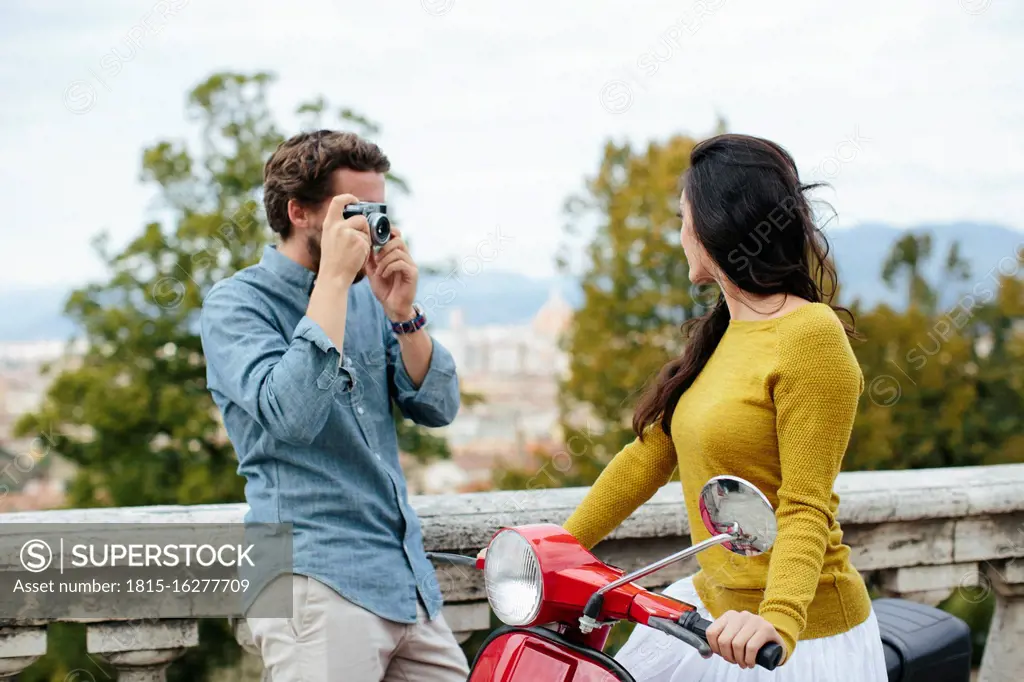 Young man photographing girlfriend sitting on Vespa