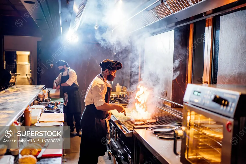 Chefs wearing protective face masks preparing a dish in restaurant kitchen