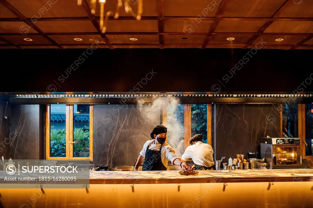 Chefs wearing protective face masks working in restaurant kitchen