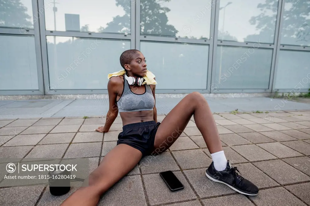 Tired female athlete with shaved head sitting on footpath in city