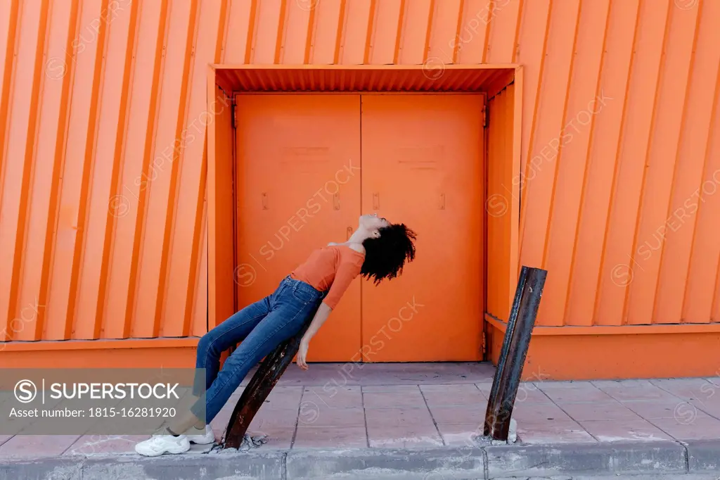 Young woman leaning on damaged metal by orange door