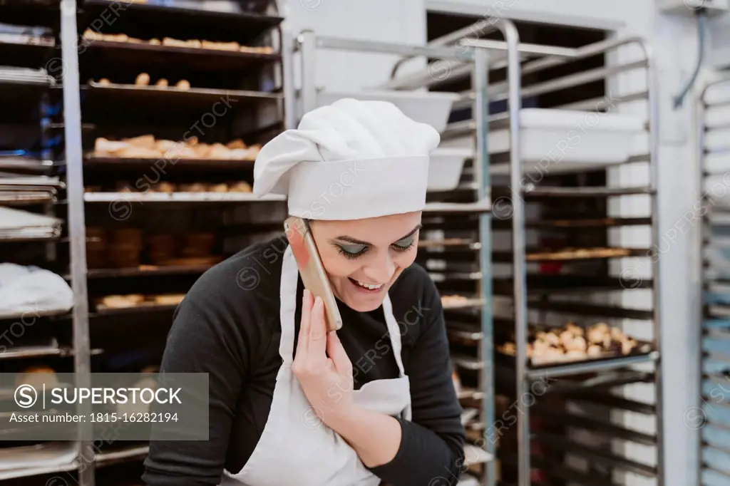 Happy female baker using smart phone in kitchen at bakery